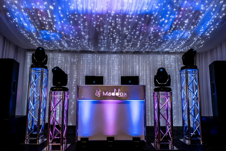 A wedding DJ setup surrounded by starlit background. Pink and blue uplighting reflect off the walls.