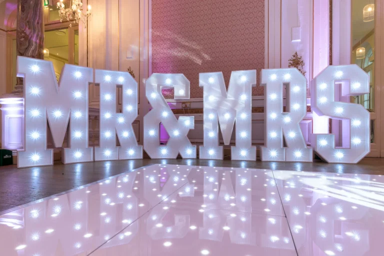 Light up Mr & Mrs giant letters. Starlit dance floor in the foreground. Venue uplighting in pink in white.