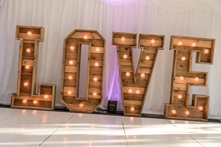 Rustic light up giant LOVE letters in wedding marquee. Venue uplighting projects pink light.