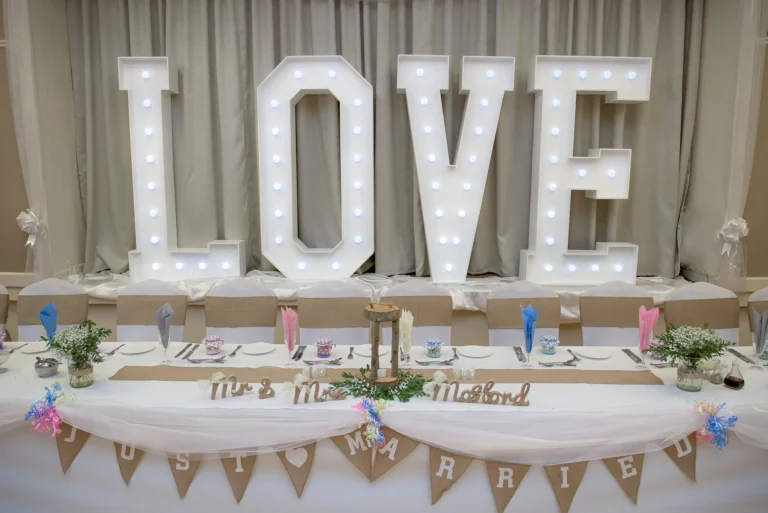 Rustic table decorations on main table at wedding reception. Giant light up LOVE letters in the background