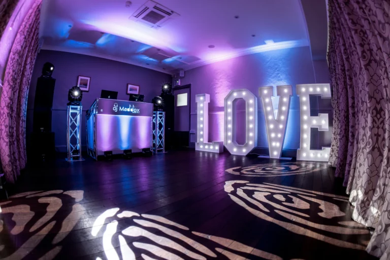 Wedding DJ setup with light up LOVE letters 5 foot high. Venue uplighting projects blue and pink light on the walls.