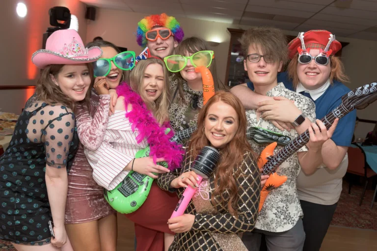 Young friends pose for a picture at a birthday party. They are having a good time and holding fun props including hats, wigs and glasses.
