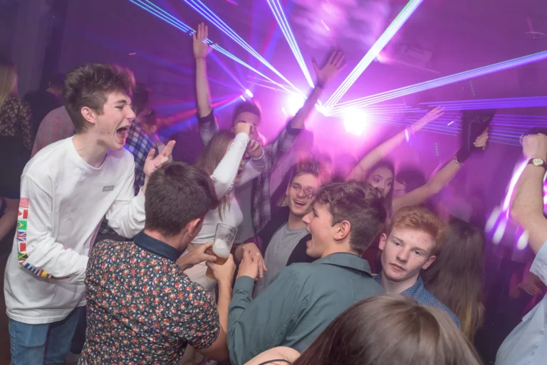 Photo of crowd jumping and shouting at 21st birthday party. Friends are having a good time. Disc Jockey is playing music.