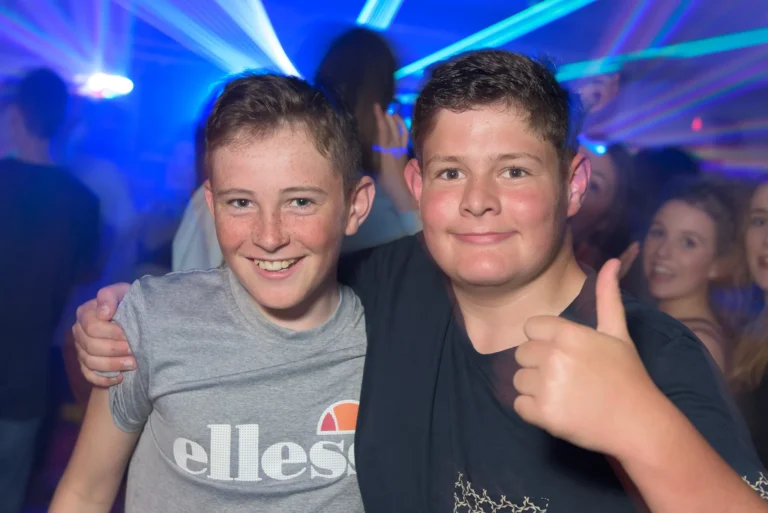 2 Children smiling for picture at birthday party. Mobile disco lights and party goes hacing a good time in the background.