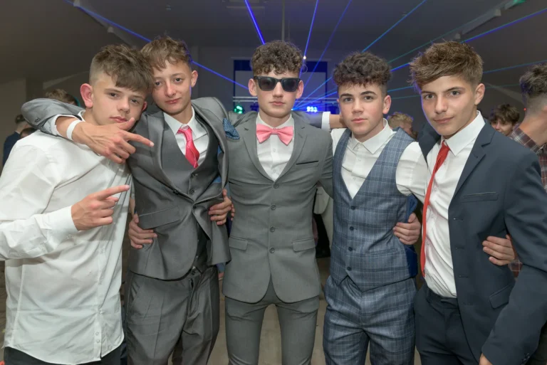 A group of smartly dressed students pose for a prom picture. In the background blue laser beams are projected from a mobile disco setup.