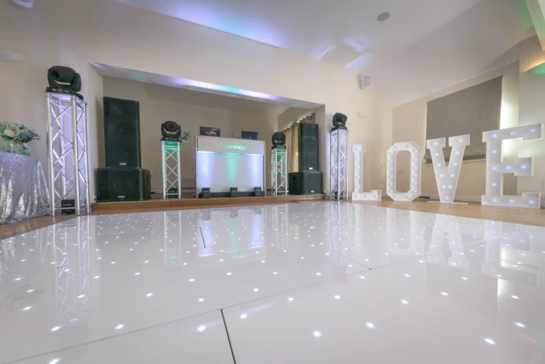 Wedding reception room with LED starlit dance floor and wedding DJ setup. Green and white uplighting illuminate the room.