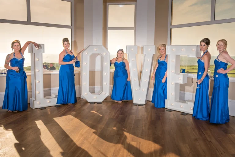 Bridesmaids posing for photo between giant LED LOVE letters at wedding venue.